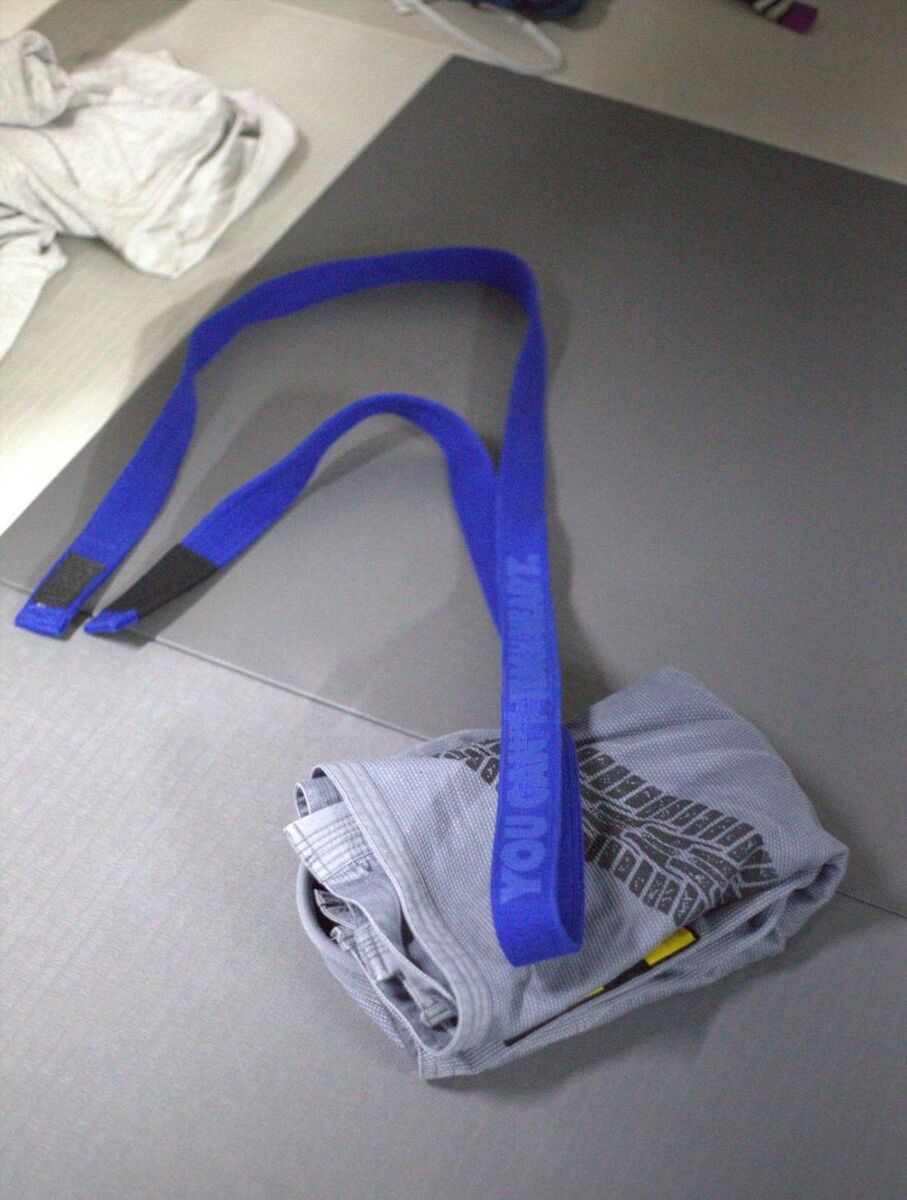 A jiu-jitsu gi folded on the mat with a blue belt — CleanMat Solutions serves BJJ and MMA academies.